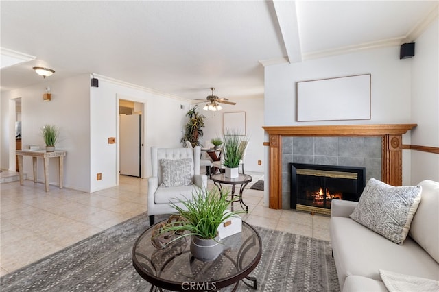 tiled living room with ceiling fan, a tile fireplace, and crown molding