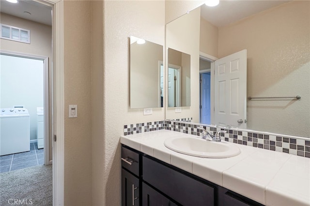 bathroom featuring vanity, washer / dryer, tile patterned floors, and decorative backsplash