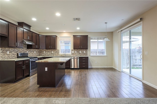 kitchen with pendant lighting, appliances with stainless steel finishes, dark hardwood / wood-style floors, light stone countertops, and a kitchen island