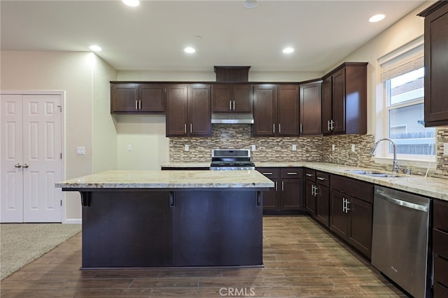 kitchen with dark wood-type flooring, appliances with stainless steel finishes, a center island, and light stone counters