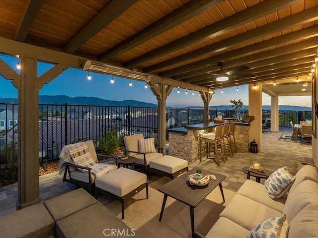 patio terrace at dusk with an outdoor living space, a mountain view, and exterior bar