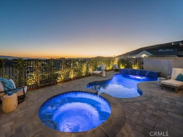 pool at dusk featuring an in ground hot tub, pool water feature, and a patio