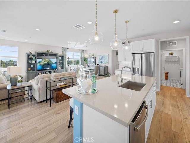 kitchen with sink, appliances with stainless steel finishes, an island with sink, pendant lighting, and white cabinets