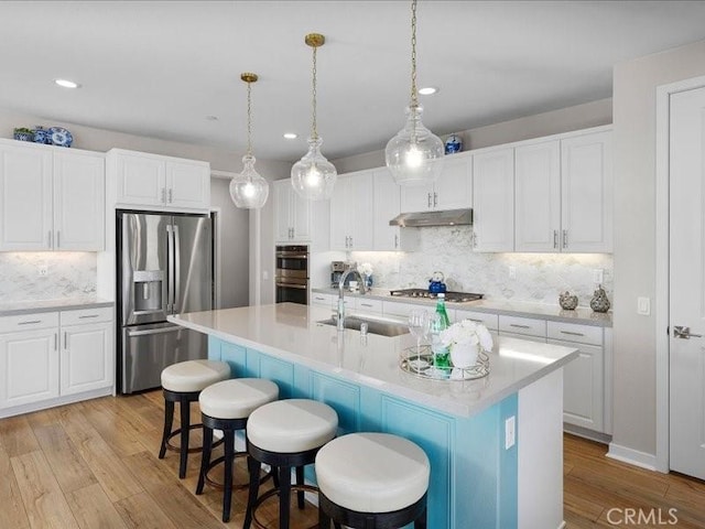 kitchen featuring a kitchen island with sink, sink, stainless steel appliances, and white cabinets