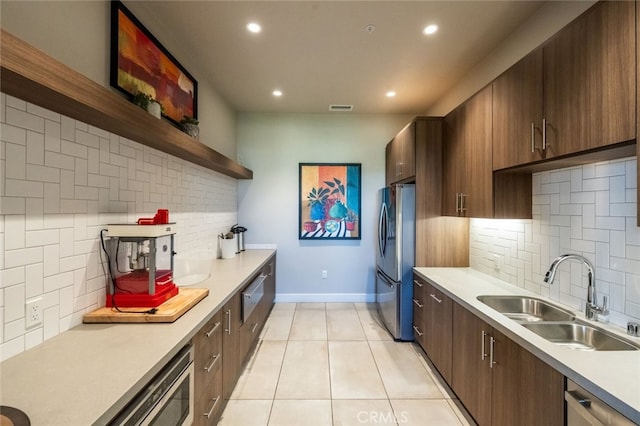 kitchen with sink, light tile patterned floors, appliances with stainless steel finishes, backsplash, and dark brown cabinetry