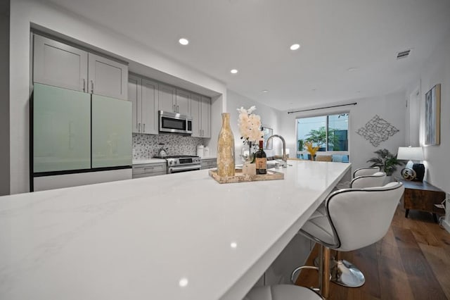 kitchen with stainless steel appliances, gray cabinetry, backsplash, a kitchen breakfast bar, and sink