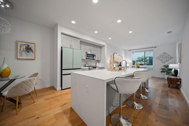 kitchen with light hardwood / wood-style floors, a center island with sink, stainless steel appliances, tasteful backsplash, and a kitchen breakfast bar