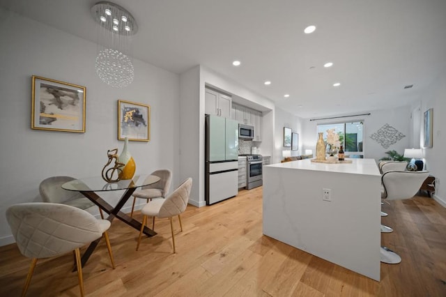 kitchen featuring stainless steel appliances, tasteful backsplash, light wood-type flooring, hanging light fixtures, and white cabinets