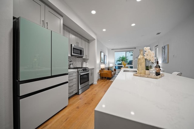 kitchen with tasteful backsplash, light wood-type flooring, gray cabinets, and stainless steel appliances