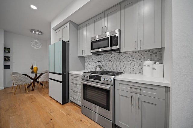 kitchen with stainless steel appliances, gray cabinetry, light hardwood / wood-style flooring, and backsplash