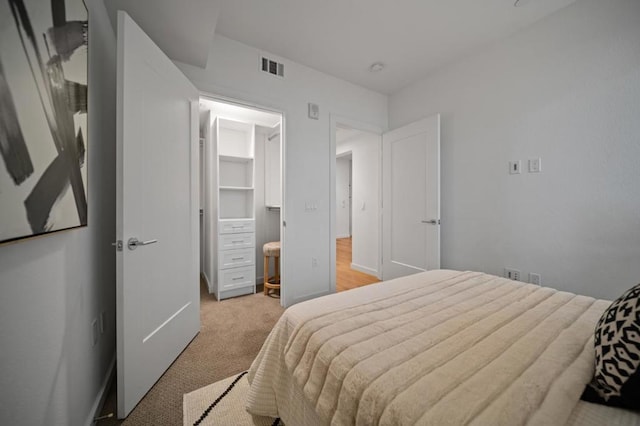 bedroom with light colored carpet and a walk in closet