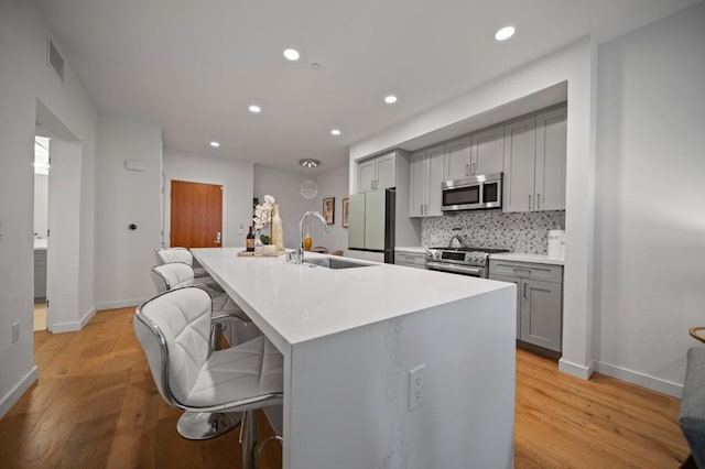 kitchen with sink, a kitchen breakfast bar, gray cabinetry, and stainless steel appliances