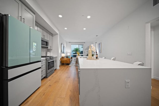 kitchen with gray cabinets, appliances with stainless steel finishes, decorative backsplash, light hardwood / wood-style flooring, and sink