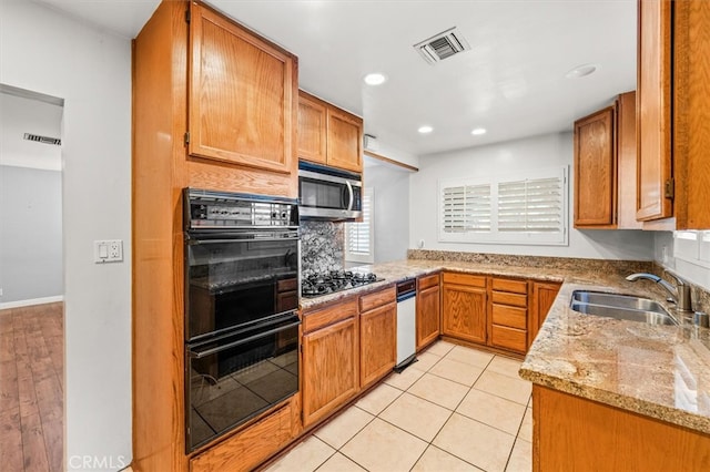 kitchen with decorative backsplash, light stone counters, light tile patterned floors, black appliances, and sink