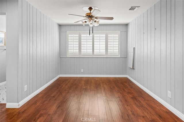 empty room featuring wood walls, ceiling fan, and dark wood-type flooring