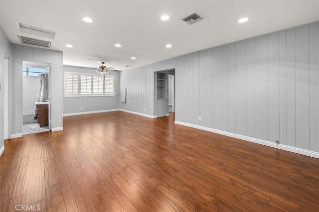 unfurnished living room featuring wooden walls, hardwood / wood-style floors, and ceiling fan