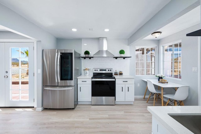 kitchen with a wealth of natural light, white cabinetry, wall chimney range hood, and appliances with stainless steel finishes