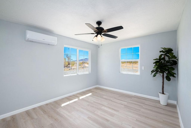 empty room with a textured ceiling, light hardwood / wood-style flooring, a wall unit AC, and ceiling fan