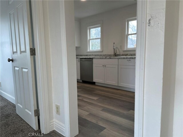 kitchen with dark wood-type flooring, white cabinets, sink, stainless steel dishwasher, and light stone countertops