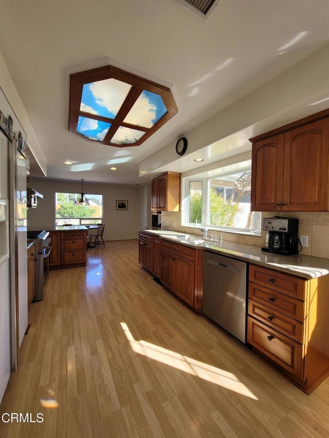 kitchen featuring pendant lighting, stainless steel appliances, light hardwood / wood-style floors, sink, and backsplash