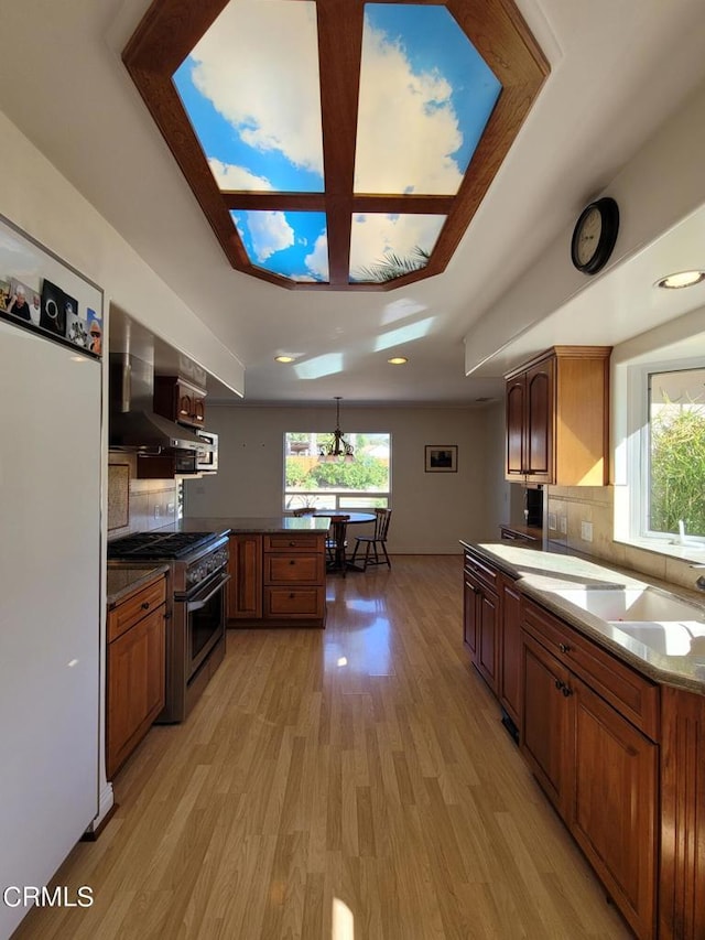 kitchen featuring high end range, wall chimney exhaust hood, decorative backsplash, light hardwood / wood-style floors, and kitchen peninsula