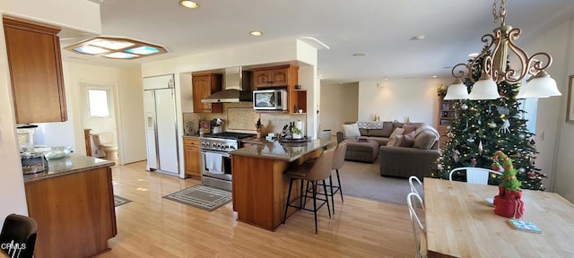 kitchen featuring appliances with stainless steel finishes, wall chimney range hood, a kitchen breakfast bar, backsplash, and light wood-type flooring