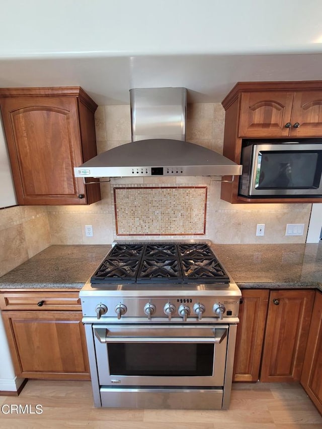 kitchen featuring appliances with stainless steel finishes, wall chimney exhaust hood, light hardwood / wood-style flooring, and tasteful backsplash