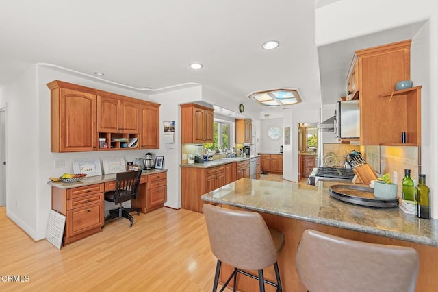 kitchen featuring light stone counters, a breakfast bar, a peninsula, light wood-style flooring, and built in desk