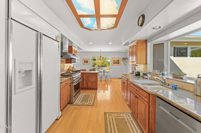 kitchen featuring light wood-type flooring, a sink, brown cabinetry, wall chimney range hood, and high end appliances