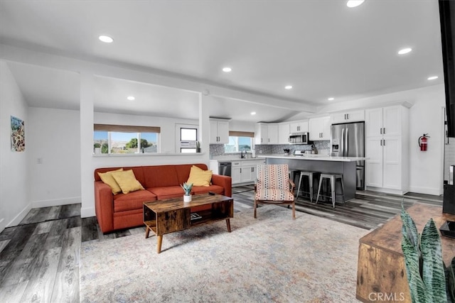 living room with wood-type flooring, beamed ceiling, a healthy amount of sunlight, and sink