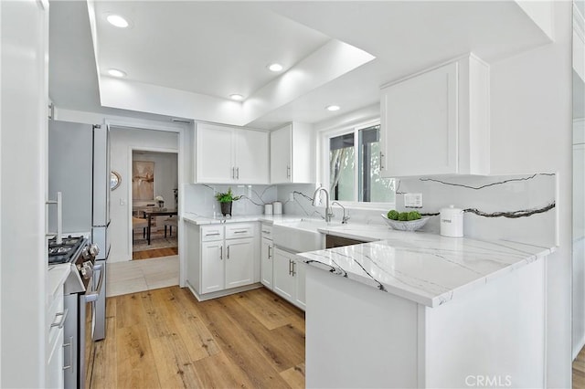 kitchen featuring a sink, a tray ceiling, stainless steel range with gas cooktop, and white cabinetry