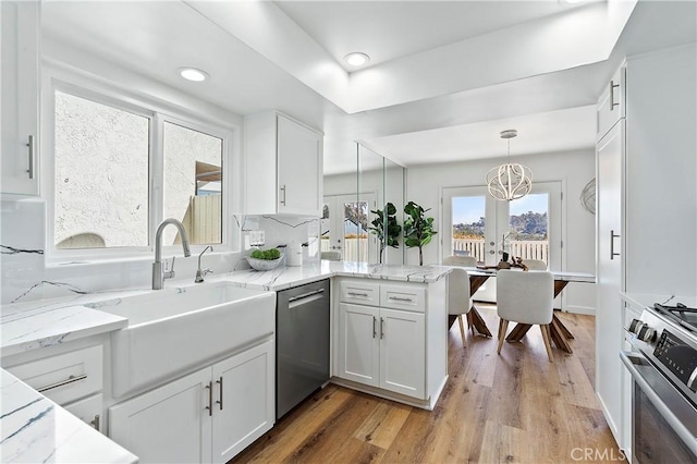 kitchen with white cabinets, a peninsula, stainless steel appliances, light wood-type flooring, and a sink