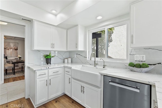 kitchen with light stone counters, stainless steel dishwasher, light wood-style floors, white cabinetry, and a sink