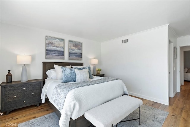 bedroom with crown molding, light wood-type flooring, visible vents, and baseboards