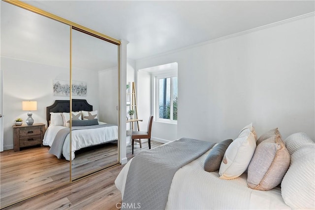 bedroom featuring ornamental molding, a closet, light wood-style flooring, and baseboards