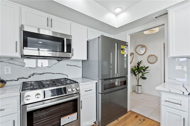 kitchen featuring appliances with stainless steel finishes, white cabinetry, visible vents, and decorative backsplash