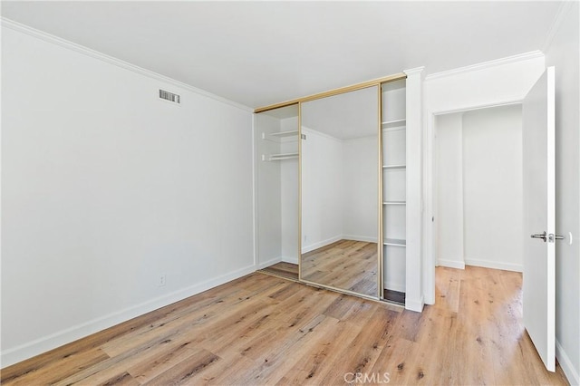 unfurnished bedroom with baseboards, visible vents, ornamental molding, wood finished floors, and a closet