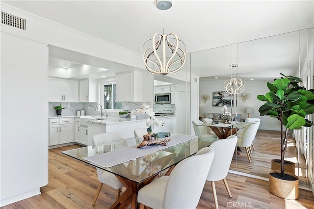 dining area featuring an inviting chandelier, light wood-style flooring, visible vents, and ornamental molding