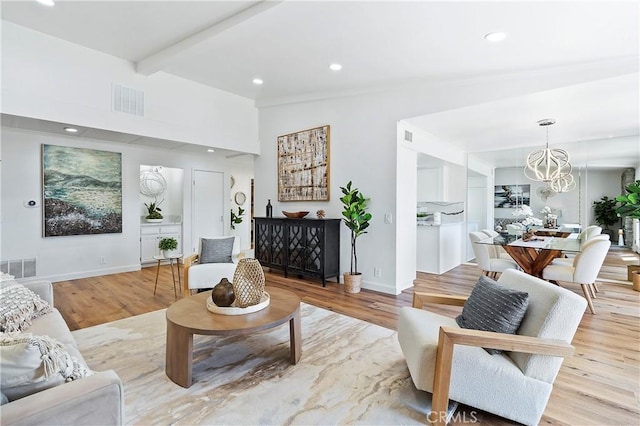 living area with light wood-type flooring, visible vents, and an inviting chandelier