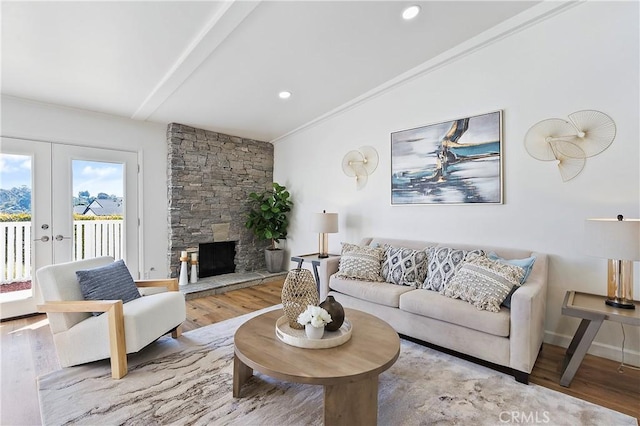 living area with french doors, ornamental molding, vaulted ceiling, a stone fireplace, and wood finished floors