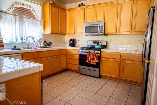 kitchen with stainless steel appliances, tile counters, light tile patterned floors, and sink