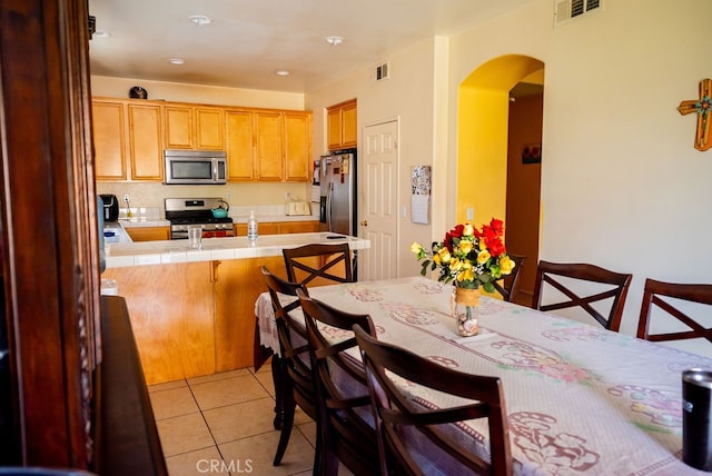 kitchen with kitchen peninsula, light tile patterned floors, stainless steel appliances, tile countertops, and a kitchen bar