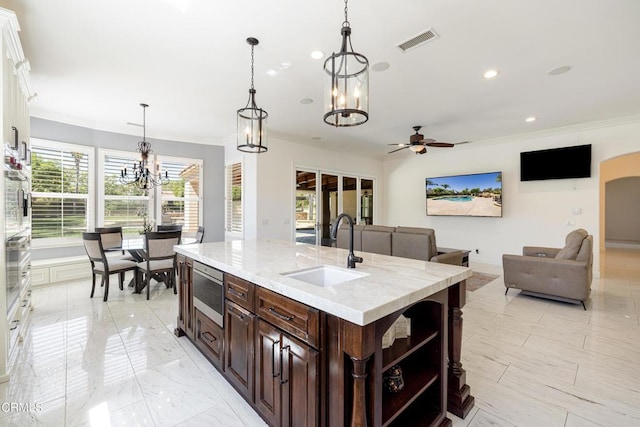 kitchen featuring pendant lighting, sink, dark brown cabinetry, an island with sink, and white cabinetry