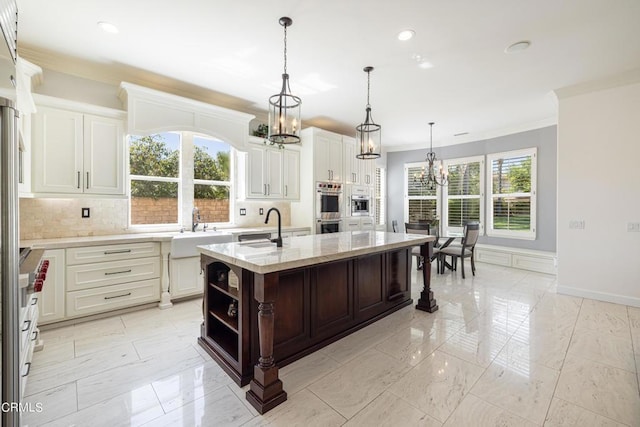 kitchen featuring a kitchen island with sink, double oven, tasteful backsplash, decorative light fixtures, and light stone counters