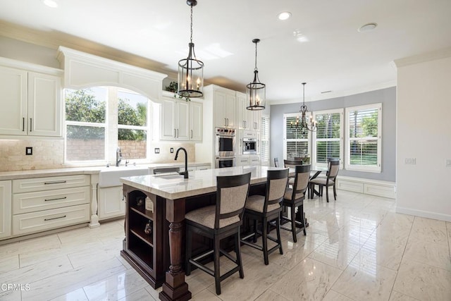 kitchen with decorative backsplash, a kitchen breakfast bar, light stone countertops, a kitchen island with sink, and sink