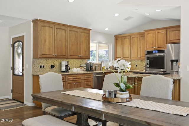 kitchen featuring light stone countertops, backsplash, stainless steel appliances, dark wood-type flooring, and lofted ceiling