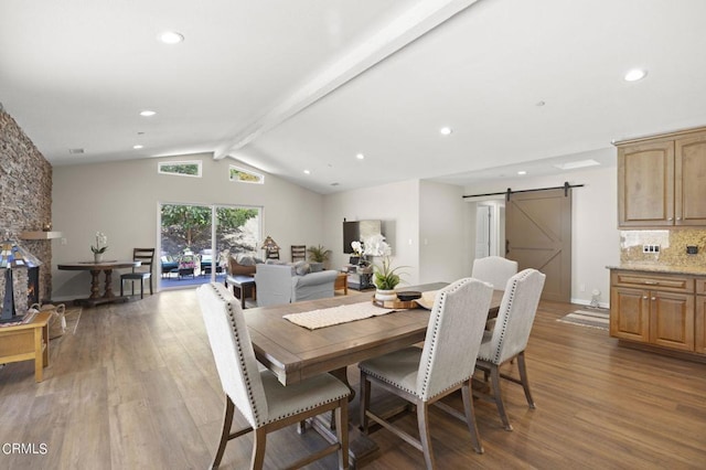 dining room featuring vaulted ceiling with beams, a barn door, and light hardwood / wood-style flooring