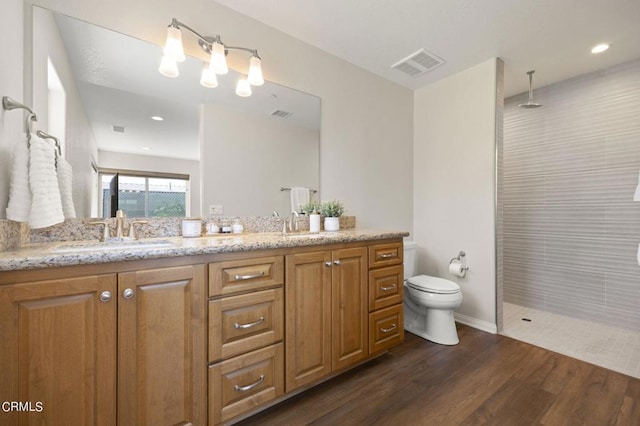 bathroom with vanity, toilet, wood-type flooring, and tiled shower