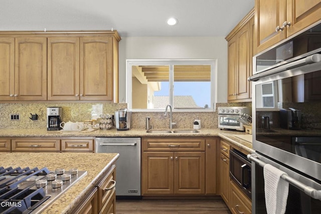 kitchen featuring sink, light stone counters, dark hardwood / wood-style floors, decorative backsplash, and appliances with stainless steel finishes