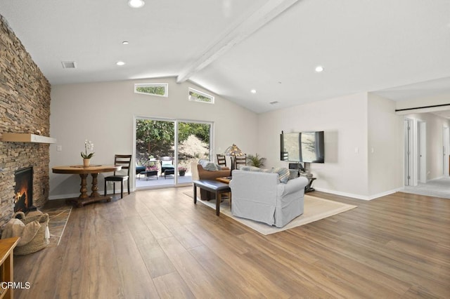 living room featuring lofted ceiling with beams, light hardwood / wood-style floors, and a stone fireplace